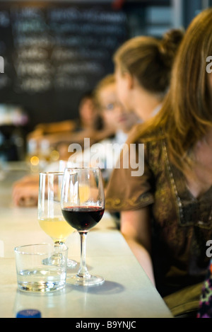 Glasses of wine set on bar, young men and women in conversation in background Stock Photo