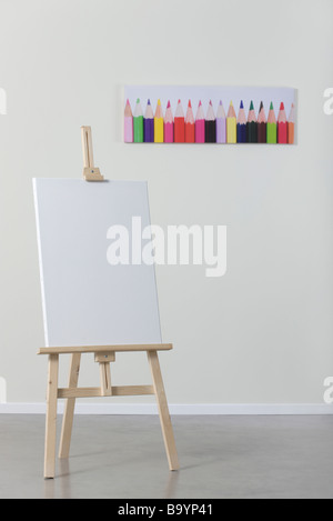 Blank canvas on easel, poster of colored pencils in background Stock Photo
