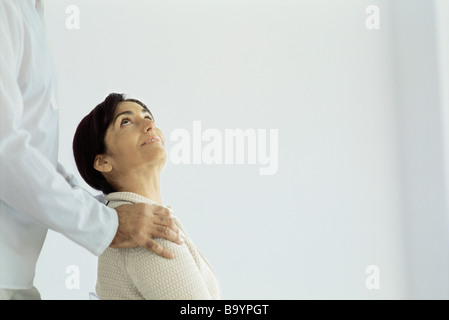 Woman sitting looking up at husband standing behind placing hands on her shoulders Stock Photo