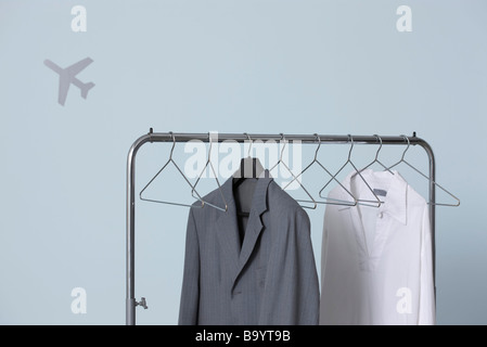 Man's formal and casual outfits hanging on clothes rack, airplane shape in background Stock Photo