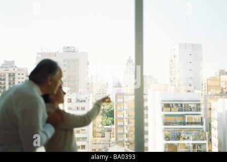 Mature couple looking out view at view of city skyline, woman pointing Stock Photo