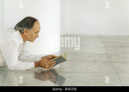 Senior man lying on tiled floor reading book Stock Photo