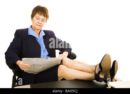 Mature business woman reading the newspaper with her feet on her desk Isolated on white  Stock Photo