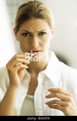Woman holding pill, frowning at camera Stock Photo