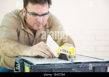 Tile worker cutting ceramic tiles with a table saw Shallow depth of field with focus on hands and blade  Stock Photo