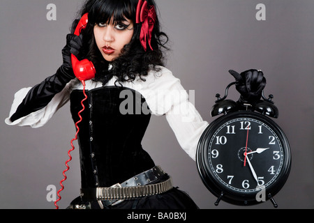 Young female holding a  alarm clock and talking on a red retro phone Stock Photo