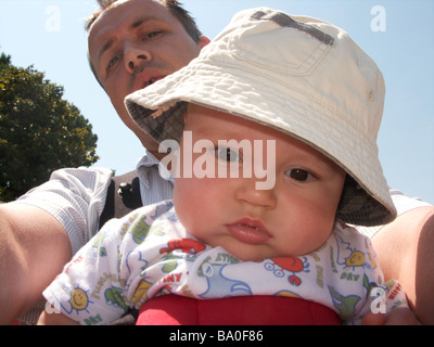 A man and baby boy with the boy looking bored wearing a cream sun hat and the man looking over is shoulder Stock Photo