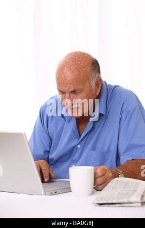 Senior man working on laptop with coffee and newspaper Stock Photo