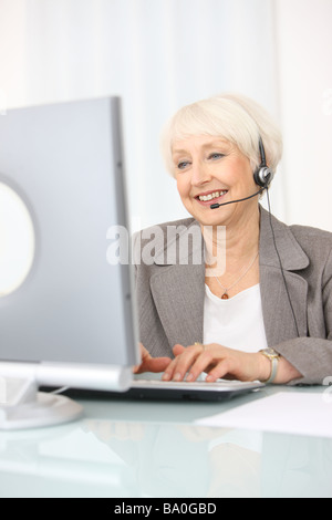 Professional senior businesswoman working on computer with headset Stock Photo