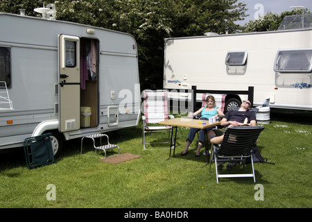 Three people relaxing in the sunshine outside a touring caravan while on holiday at a site near Port Eynon South Wales UK Stock Photo