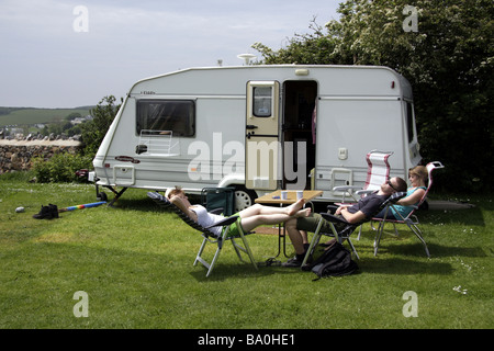 Three people relaxing on holiday outside a touring caravan at a caravan site near Port Eynon, South Wales Stock Photo