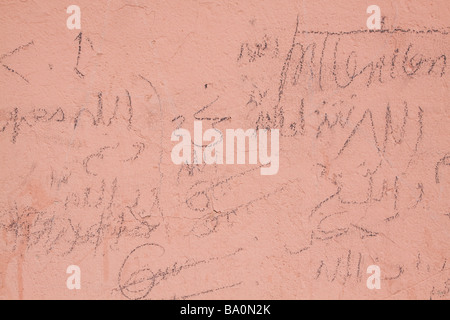 Hand written graphitti and messages written in arabic drawn over a salmon pink coloured typical wall in Marrakech Stock Photo