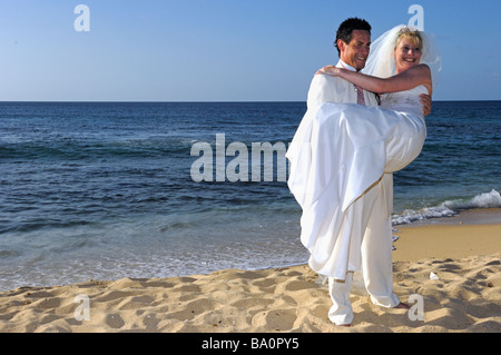 Groom carrying new bride on tropical sandy Caribbean beach Grenada Stock Photo