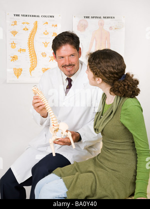 Friendly smiling chiropractor uses a model to explain the spinal nervous system to a patient  Stock Photo