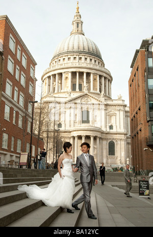an oriental asian bride and groom holding hands on steps near St Pauls Cathedral London Stock Photo