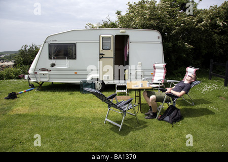 A teenage boy relaxing in the sunshine outside a touring caravan at a caravan site near the sea at Port Eynon South Wales. Stock Photo