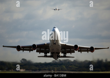 Virgin Atlantic Boeing 747 Jet Airplane takes off from Gatwick airport West Sussex with a smaller jet coming into land behind Stock Photo