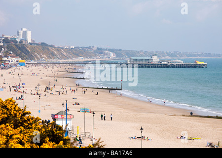 Bournemouth Pier and golden sandy beach with hotels in distance and people sunning themselves with blue sky and sea and cliffs Stock Photo