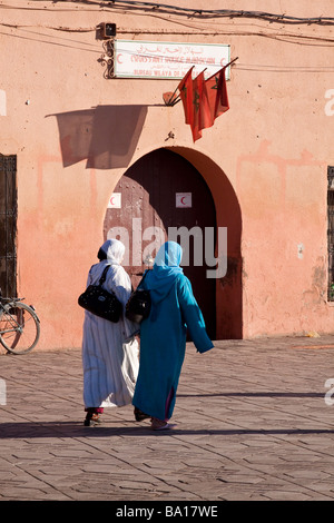Two arab musim women in traditional clothing dress walk past colourful entrance to a small mosque with Moroccan flag displayed Stock Photo