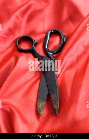 Old rusty pair of scissors on a red silk material Stock Photo