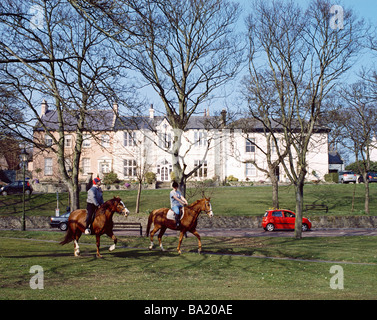 Two young women riding horses through Whitburn Village near Sunderland north east England, UK Stock Photo