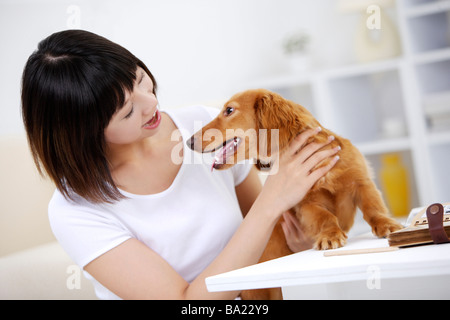 Young woman playing with Dachshund at table smiling Stock Photo