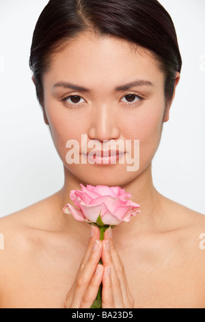 Studio shot of a beautiful young Japanese woman holding a pink rose between her clasped hands while in meditative contemplation Stock Photo