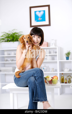 Young woman sitting embracing Dachshund looking at camera smiling Stock Photo