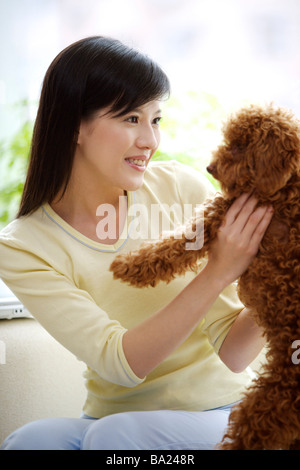 Young woman holding Toy Poodle on sofa close up Stock Photo