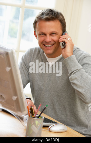 Man Using Computer And Talking On Phone Stock Photo