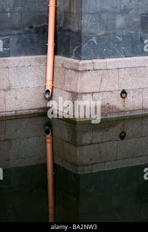 Drain pipe on granite wall over water. Stock Photo