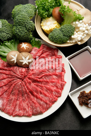 Slices of raw beef on plate pot of vegetables aside Stock Photo