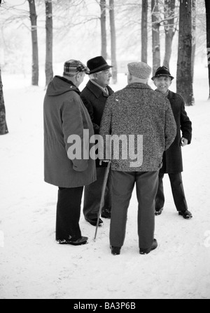 Seventies, black and white photo, people, four older men take a walk, retired persons, winter, snow, walking stick, aged 65 to 75 years Stock Photo