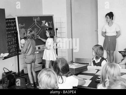 Seventies, black and white photo, edification, school, schoolboys and schoolgirls in a school class during lessons, woman teacher, children aged 7 to 10 years, boy and girl at a blackboard Stock Photo