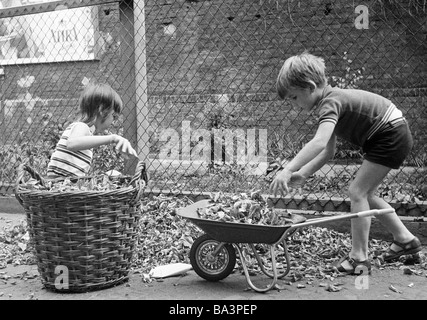 Seventies, black and white photo, people, children, little girl and little boy collecting autumn leaves in a basket and with a wheel-barrow, aged 4 to 7 years Stock Photo