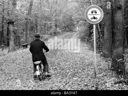 Seventies, black and white photo, autumn, forest, forest road, prohibition sign, no entry for motorcars and motorbikes, nevertheless an older man on a moped passes through, aged 60 to 70 years, D-Bottrop, D-Bottrop-Kirchhellen, Grafenwald, Ruhr area, North Rhine-Westphalia Stock Photo