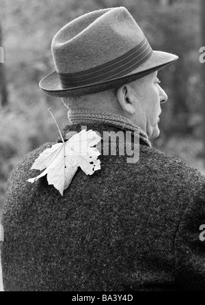 Seventies, black and white photo, autumn, symbolic, older man with scarf and hat, rear view, an autumn leaf on his shoulder, aged 60 to 70 years Stock Photo