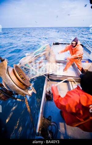 Deckhands lower a baited pot over the deck of the F/V Centurion while cod fishing in Kachemak Bay, Alaska Stock Photo