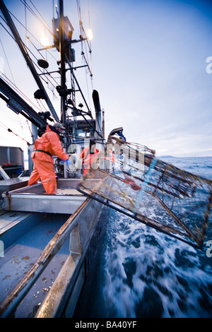 Deckhands lower a baited pot over the deck of the F/V Centurion while cod fishing in Kachemak Bay, Alaska Stock Photo