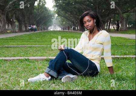 Young Woman Sitting In Park Wearing Headphones Listening To Music On Mp3 Player Stock Photo