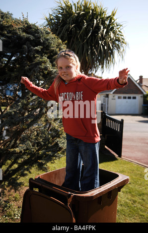Young 9 yr old girl jumps up and down in a council garden recycling waste bin UK Stock Photo