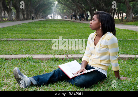 Young Woman Sitting In Park Reading A Text Book Studying Stock Photo