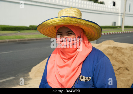 Portrait of a female Thai road worker wearing a protective pink face scarf and straw hat in a  Bangkok street Stock Photo