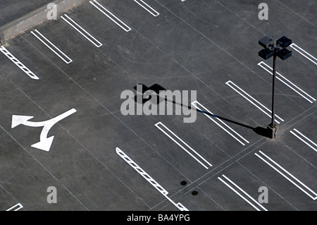 Black and white image of overhead, graphic shot of a freshly painted parking lot with light pole, arrows and dramatic shadow. Stock Photo