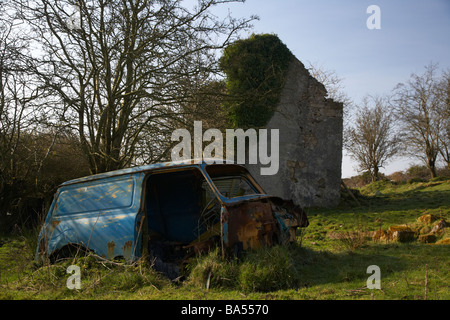 old blue rusted abandoned wreck of an old mini van in a field next to an old abandoned farmhouse in county armagh ireland Stock Photo