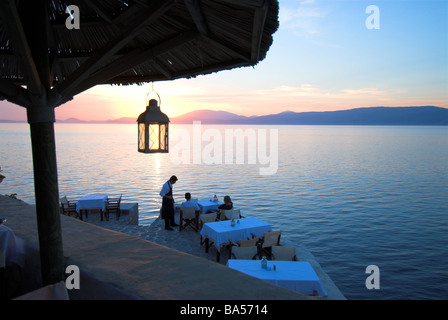 Diners and waiter at a seaside restaurant at dusk, Hydra, Greece Stock Photo