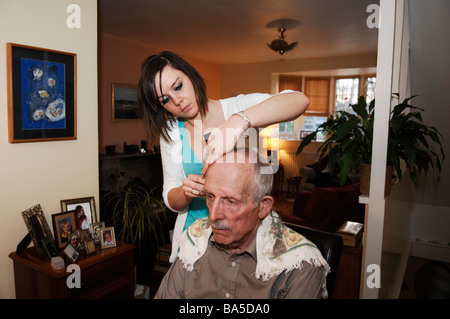 Hairdresser cutting her grandfathers grey hair at home Stock Photo