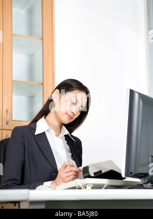 Businesswoman sitting at desk checking schedule book Stock Photo