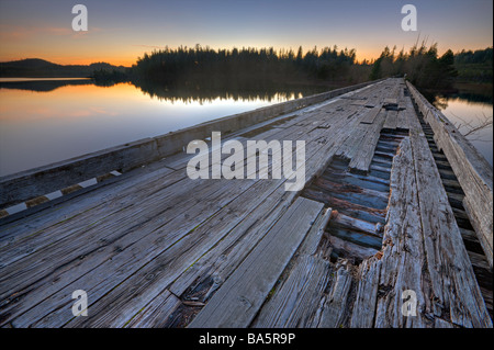Old wooden bridge spanning the entrance to Clayoquot Arm of Kennedy Lake at sunset, a transition area of the Clayoquot Sound. Stock Photo