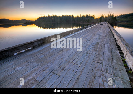 Old wooden bridge spanning the entrance to Clayoquot Arm of Kennedy Lake at sunset, a transition area of the Clayoquot Sound. Stock Photo